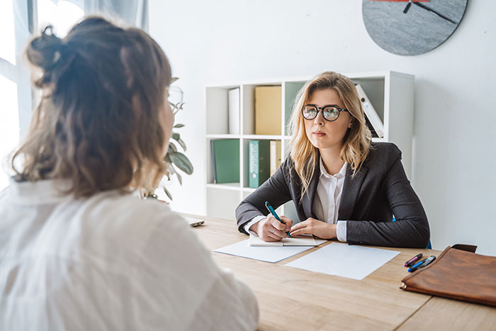 Woman in glasses discussing inheritance embezzlement and gaslighting in a bright office setting with another woman.
