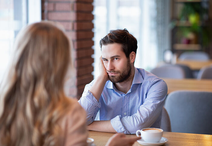 A man looking uninterested and unattractive during a tense conversation with a woman in a cozy cafe setting.