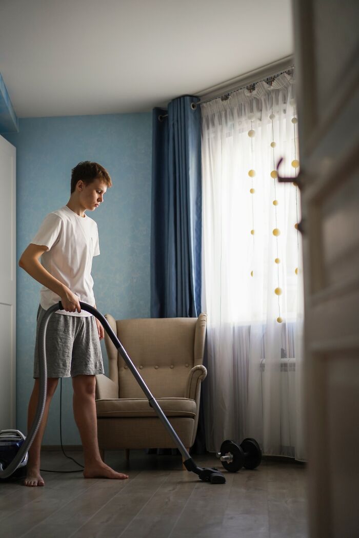 Teen boy vacuuming floor in living room, illustrating parents punishing kids by leaving them alone for days with no food