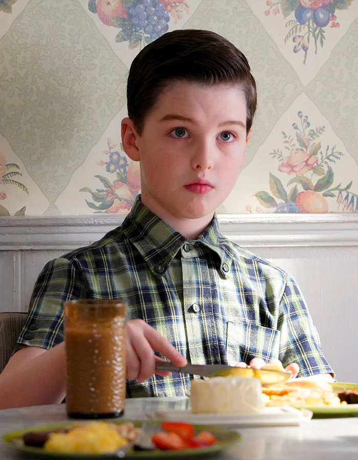 Young Sheldon child star sitting at breakfast table with plaid shirt, fans remarking he looks like Tom Cruise after growing up