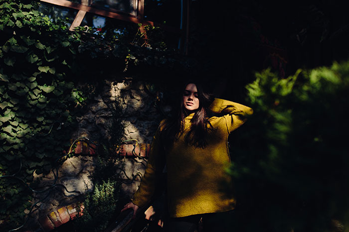 Pregnant woman in yellow sweater standing near house wall with vines, looking concerned after spotting neighbor lurking nearby. - 22