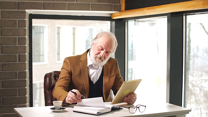 Older man in a brown jacket reviewing documents at a desk, reflecting on DNA test results about his son. Older man in a brown jacket reviewing documents at a desk, reflecting on DNA test results about his son.