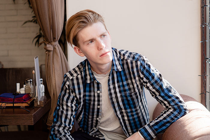 Young man in a checkered shirt sitting on a couch, looking pensive after DNA results reveal golden child status. Young man in a checkered shirt sitting on a couch, looking pensive after DNA results reveal golden child status.