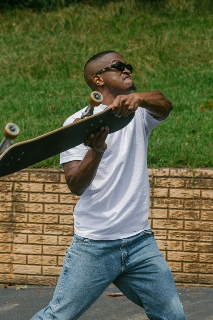 Man in sunglasses holding skateboard aggressively outdoors, illustrating hard-to-believe stories shared by people.