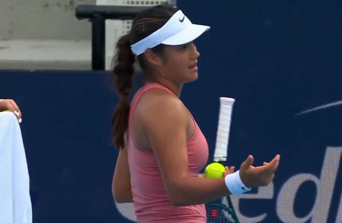 Tennis star in pink outfit holding tennis ball and racket, showing frustration during match pause over crying baby incident.
