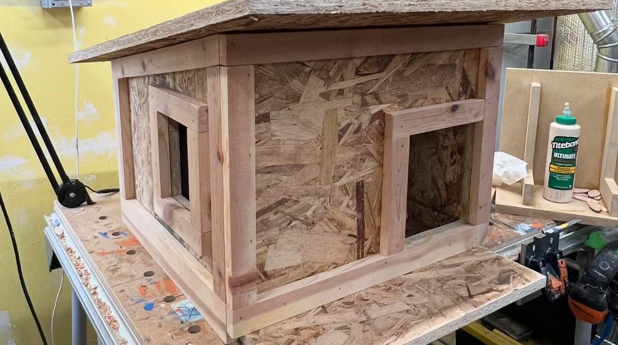 Handcrafted wooden cat house with open windows in a workshop, built for a tuxedo cat sleeping on a porch. Handcrafted wooden cat house with open windows in a workshop, built for a tuxedo cat sleeping on a porch.