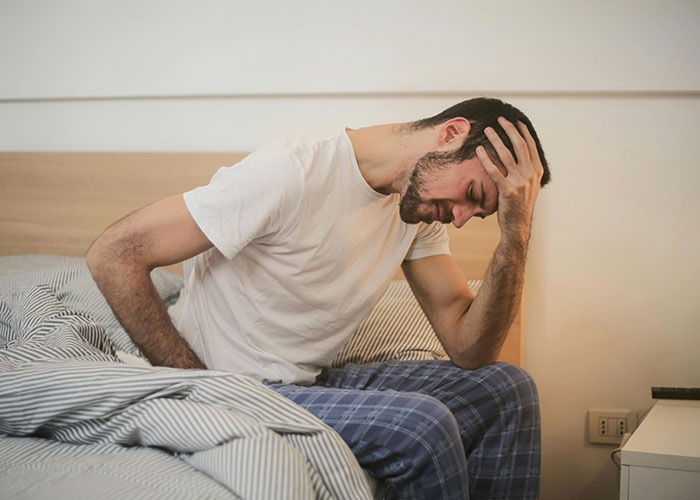 Man sitting on bed holding stomach and head, appearing sick after eating food his dad has touched.