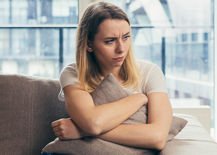 Frustrated woman sitting indoors hugging a pillow, reflecting the stress of a mom taking kids on a 9-hour flight.