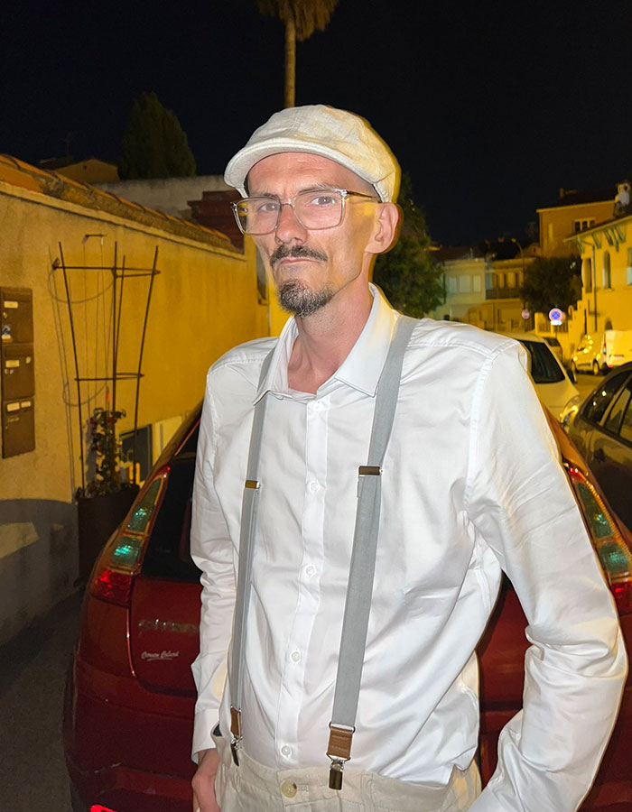 Man wearing a white shirt, suspenders, and cap standing outside at night after streamer's horrifying passing live on-air. Man wearing a white shirt, suspenders, and cap standing outside at night after streamer's horrifying passing live on-air.