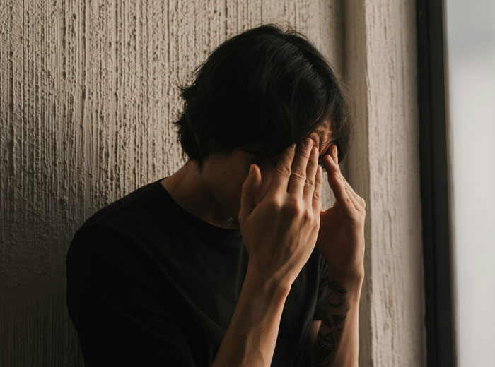 Teen holding head in hands near wall, showing stress and conflict over keeping late father's last name.
