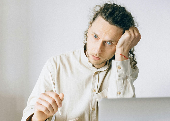 Pensive intern sitting at laptop, looking stressed and distracted after coworker brings cupcakes to workplace.