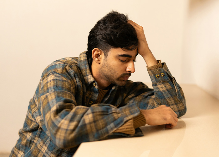 Young man wearing plaid shirt sitting quietly with head resting on hand, representing a silent deaf man in a thoughtful moment