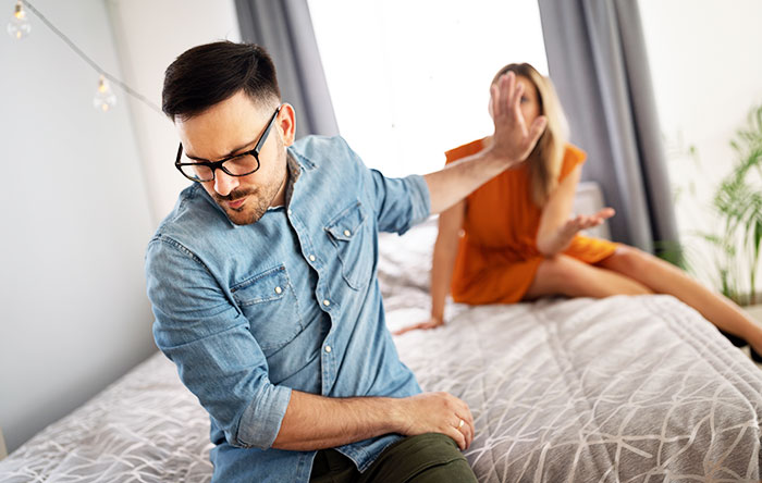 Man in denim shirt refusing to talk, turning away from woman on bed, depicting marriage conflict and family issues.