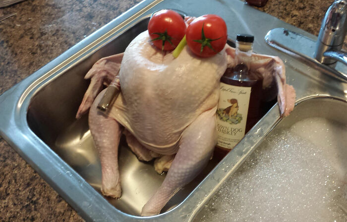 Raw chicken posed with tomatoes and bottles in a kitchen sink, showing a weird thing seen in someone else’s home. - 8