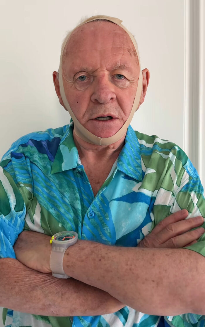 Anthony Hopkins wearing a face strap, parodying a viral beauty product in a colorful shirt with arms crossed.