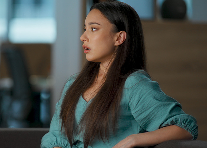 Young woman with long hair in a teal blouse showing a shocked expression representing moments rich people realize lifestyle differences - 6