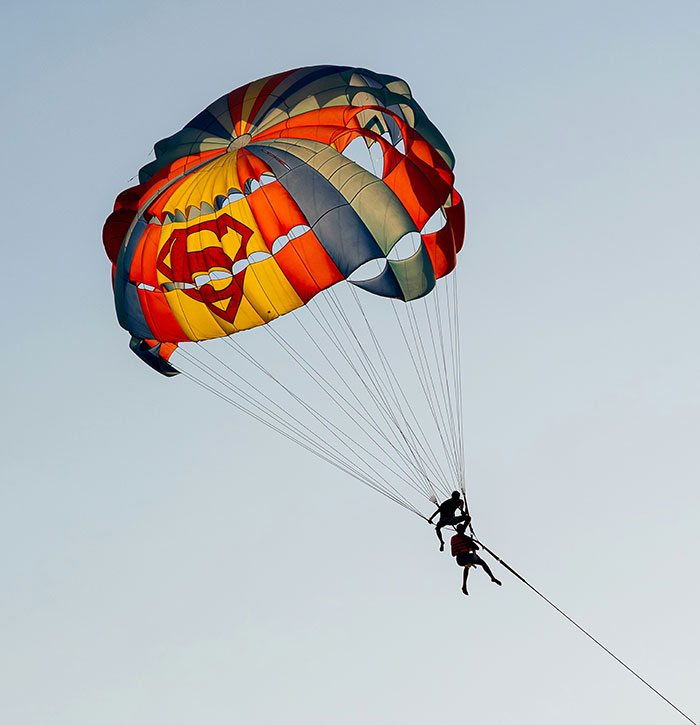 Two people parasailing mid-air with a colorful parachute against a clear sky, highlighting parasailing assault risk. - 1