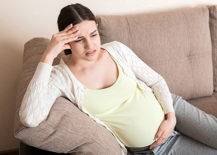 Pregnant woman looking worried and holding her belly on a couch, illustrating regret from ignoring gut feelings.
