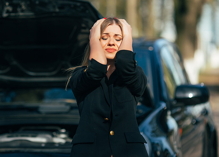 Woman holding her head in distress next to a broken-down car, illustrating regret after ignoring a gut feeling.