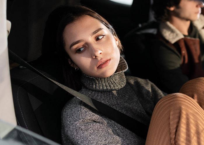 Young woman wearing a seatbelt, looking worried inside a car, illustrating moments of ignoring gut feelings and regret.