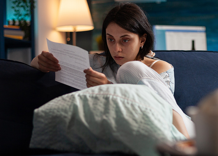 Woman sitting on a couch looking worried while reading a document, illustrating gut feeling regret and lucky to be alive.