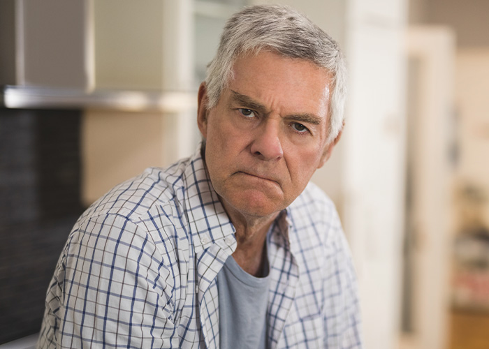 Elderly man with serious expression reflecting on gut feeling regret in a home setting, illustrating lucky to be alive theme.