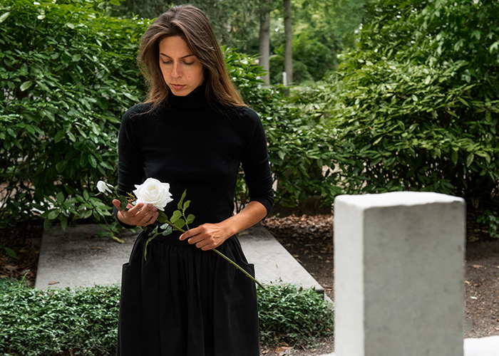 Woman in black holding white rose, standing thoughtfully near a grave, reflecting on gut feelings and regret.
