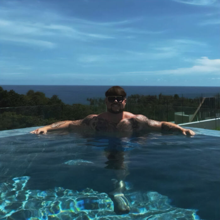 Ibiza Final Boss relaxing in a pool with sunglasses, showcasing a viral haircut against a clear sky and ocean backdrop. Ibiza Final Boss relaxing in a pool with sunglasses, showcasing a viral haircut against a clear sky and ocean backdrop.