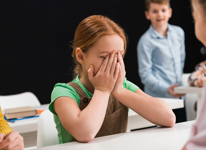 Young girl covering her face in embarrassment while other children react, illustrating stories of people getting savagely rejected.