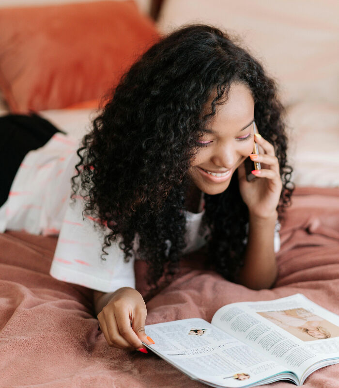 Smiling woman with curly hair reading a magazine and talking on the phone, illustrating Reddit not for the faint of heart.