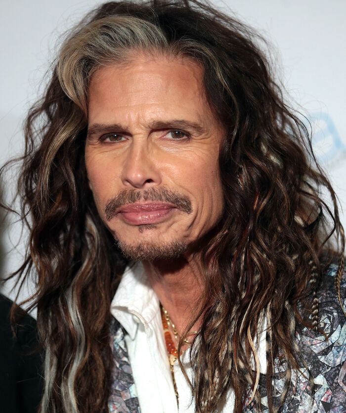 Man with long curly hair and a mustache, wearing a patterned jacket, illustrating new facts for learning enthusiasts.