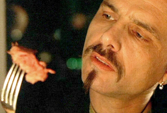 Man with goatee and earring examining a piece of food on a fork, curious and focused on learning new facts.