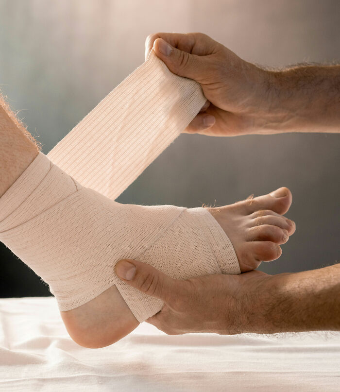 Person wrapping an ankle with a bandage demonstrating care for the human body and its healing process.