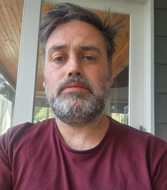 Middle-aged man with beard and maroon shirt at home, representing caf&eacute; owner addressing entitled customers and teen worker issues.