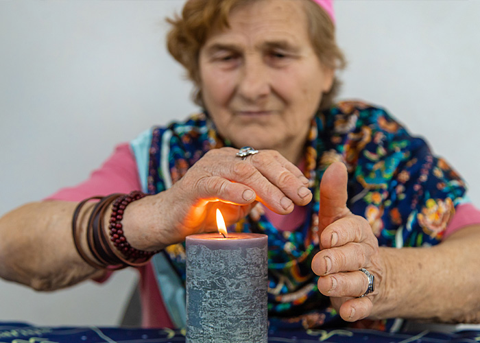 Elderly woman warming hands over a burning candle, illustrating common causes of house fires and fire safety risks.