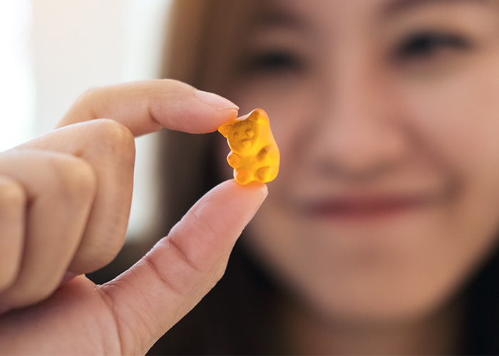 Person holding a small gummy bear candy close to the camera with a blurred face in the background, illustrating house fire risks.