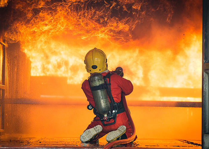Firefighter in full gear battling a large house fire caused by a Roomba knocking over a candle.