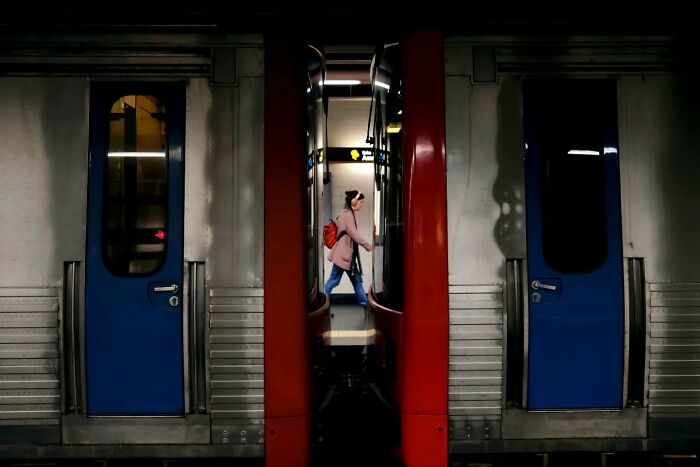 Person with red backpack walking through a subway platform, capturing life’s unseen unposed moments on the streets.