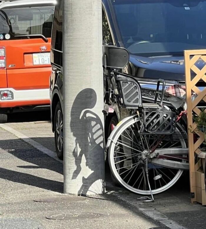 Shadow of a bicycle on a pole creating a random object that looks like a face in a street parking area.