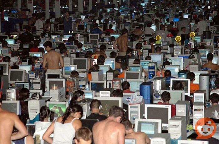 Large crowded room filled with people using old computers, showcasing unfamiliar parts of history through vintage technology.