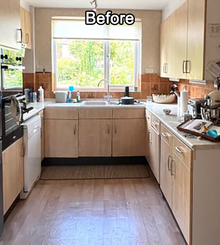 Kitchen before DIY makeover showing outdated cabinets, appliances, and clutter with natural light from a window above the sink.