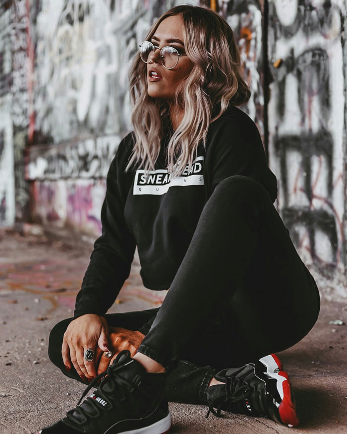 Young woman wearing sneakers and casual black clothing sitting by graffiti wall showing things Americans do that make them stand out abroad