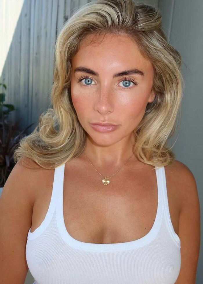 Blonde woman with blue eyes wearing a white tank top and gold necklace, related to Taylor Swift furious over Bonnie Blue comment.