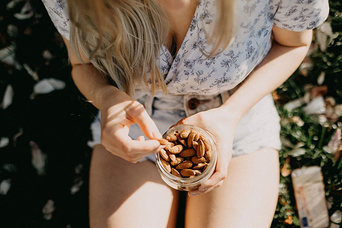 Woman holding a jar of almonds outdoors, highlighting peanut butter cake frustration from boyfriend unable to eat it.