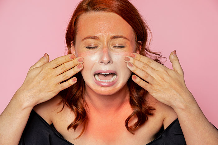 Woman upset crying with hands near face against pink background, illustrating frustration over peanut butter cake at work.