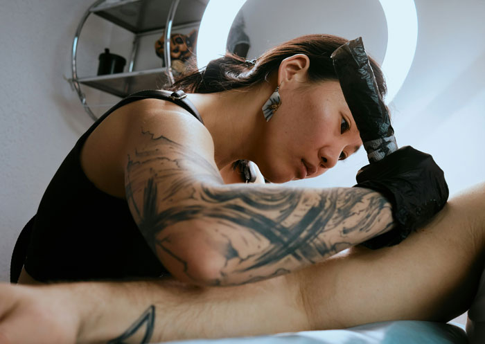 Tattoo artist with sleeve tattoo carefully working on a client’s leg, capturing unhinged wedding spends creativity and detail. - 34