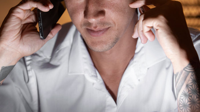 Man in white shirt with tattooed arm talking on a phone, illustrating bar staff protecting women from creepy men.