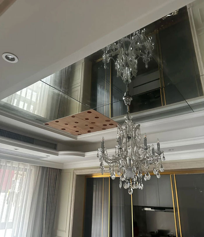 Crystal chandelier hanging from a ceiling with a broken glass panel reflecting the room interior.