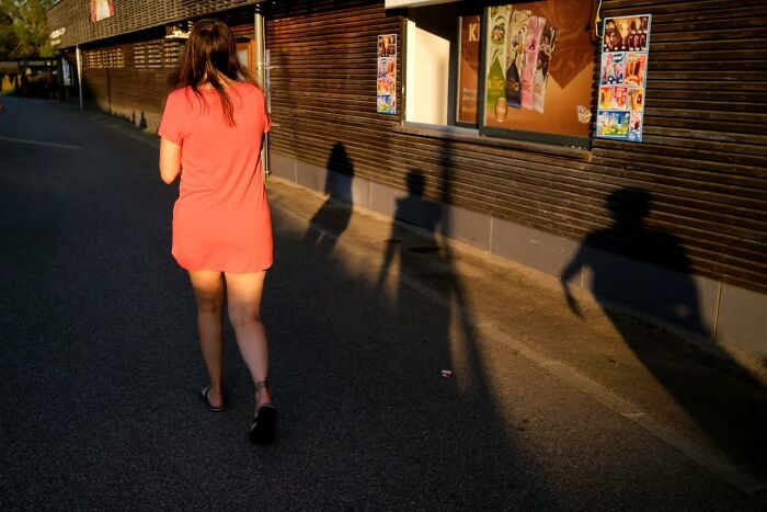 Woman walking alone on a street during golden hour, casting long shadows in a candid street moments photograph.