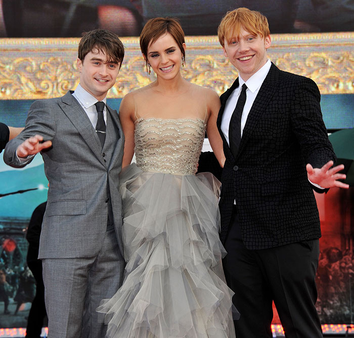 Actors Daniel Radcliffe, Emma Watson, and Rupert Grint posing together at a formal event in elegant attire.
